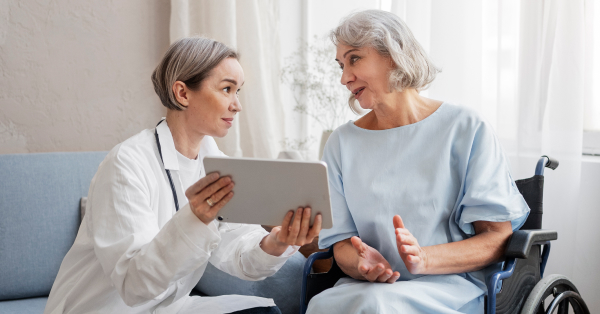Doktorica pokazuje nešto na tabletu starijoj pacijentkinji u invalidskim kolicima