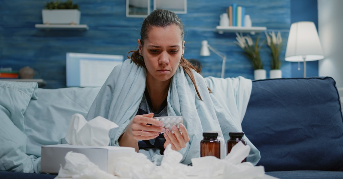 devojka na kauču sa papirnim maramicama i lekovima