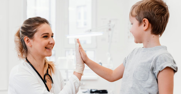 Nasmejana doktorica i dečak se pozdravljaju pljeskom dlana u vazduhu